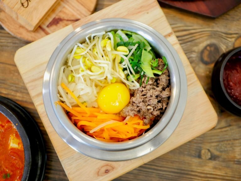 Bibimbap v miske s ryžou, špenátom, mrkvou, cuketou, hubami, hovädzím mäsom, volským okom a gochujang omáčkou